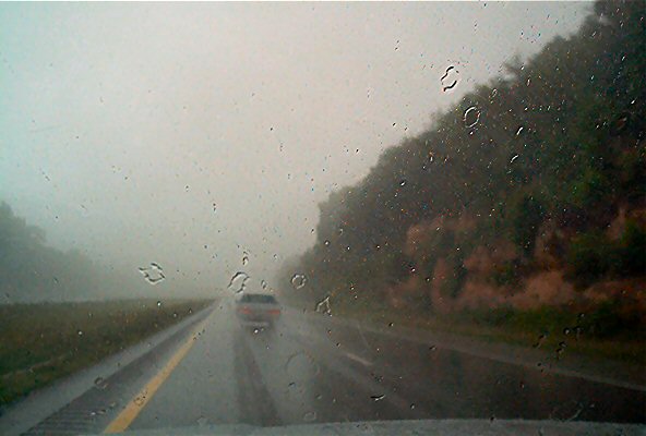 Car driving on a wet highway in the rain, seen through a rain-streaked windshield