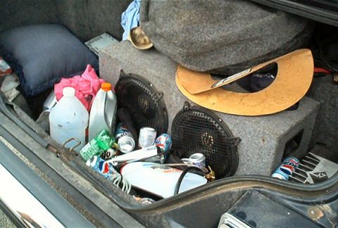 1985 Ford LTD Crown Victoria - The trunk of a car is filled with various items including speakers, cleaning supplies, and empty beverage cans.