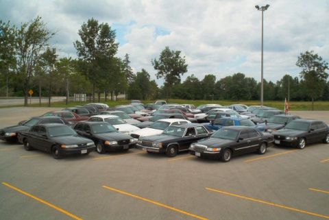 1985 Ford LTD Crown Victoria - A fleet of Ford Crown Victorias are parked in an outdoor lot under a cloudy sky.