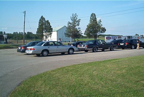 1985 Ford LTD Crown Victoria - A row of cars, including a 1985 Ford Crown Victoria LTD, parked outdoors on a sunny day.
