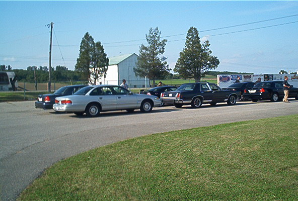 Several cars parked side-by-side, including a silver 1985 Ford Crown Victoria LTD and a dark coupe