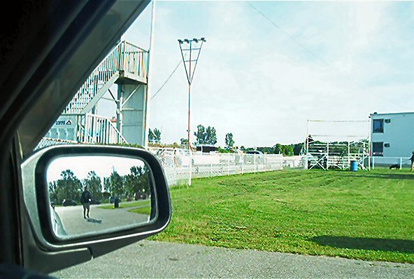 Reflection in side mirror shows a person walking on a paved path with trees behind them