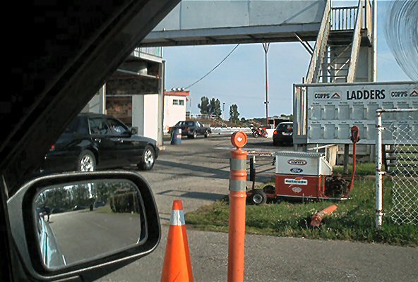 Black sedan parked near a drag strip structure, seen from driver's side