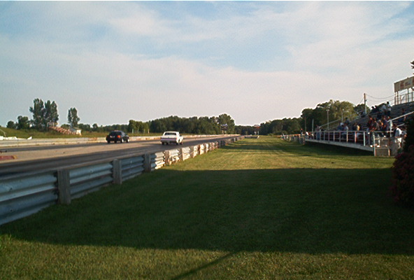 Two cars race down a drag strip with spectators in the stands