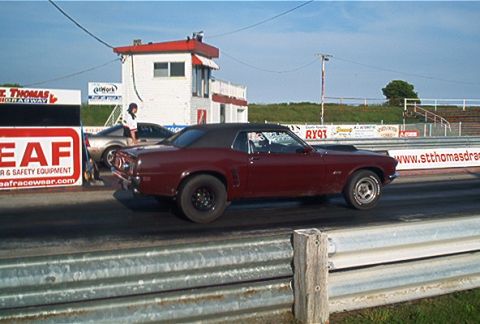1985 Ford LTD Crown Victoria - A maroon convertible muscle car competes at a drag strip alongside another vehicle.