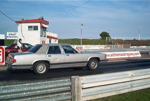 1985 Ford LTD Crown Victoria - A silver sedan is on the drag strip with a banner for st. thomas dragway in the background.