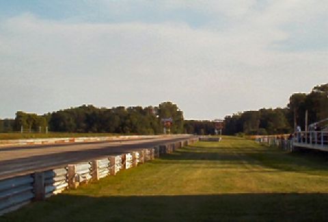 1985 Ford LTD Crown Victoria - A drag strip scene with guardrails and trees under a partly cloudy sky.