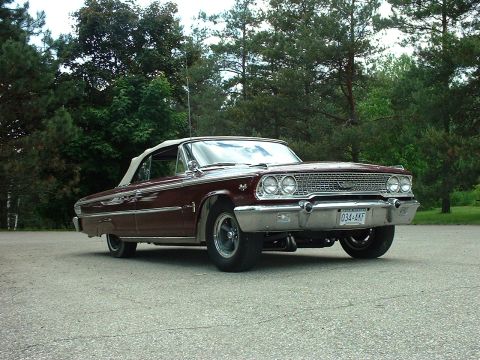 1963 Ford Galaxie - A classic 1963 Ford Galaxie convertible is shown from a three-quarter front view, parked on asphalt with a wooded area behind it.