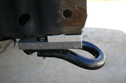 1994 Ford Bronco - Close-up of a black tow hook bolted to a rusty frame horn, with two bare steel spacer blocks stacked between the hook bracket and the frame…