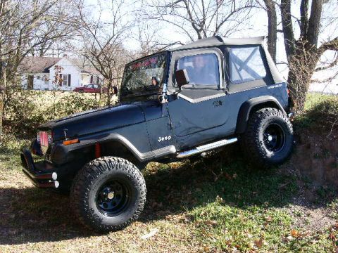 1987 Jeep Wrangler - 1987 Jeep Wrangler parked on a dirt embankment, showing its off-road tires and soft top.