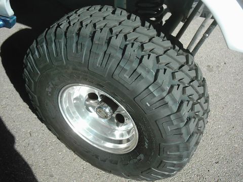 1978 Ford Bronco - A close-up view of a large, off-road tire mounted on a shiny aluminum wheel, with a portion of a white vehicle in the background.