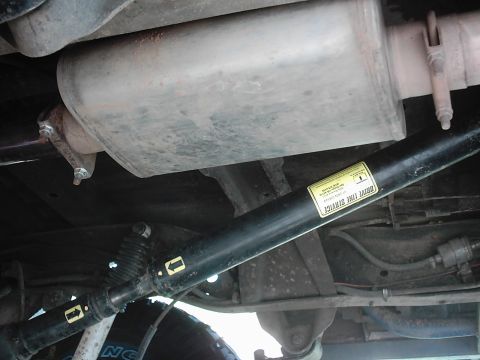 1978 Ford Bronco - Underside view of a vehicle's drive shaft and exhaust system, with a service sticker present.