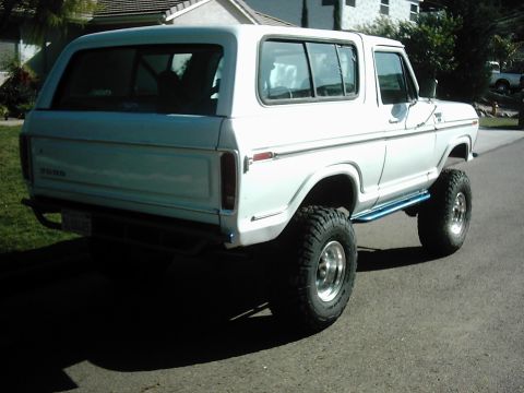 1978 Ford Bronco - This white 1978 Ford Bronco features off-road tires and blue side steps, viewed from the rear three-quarter angle.