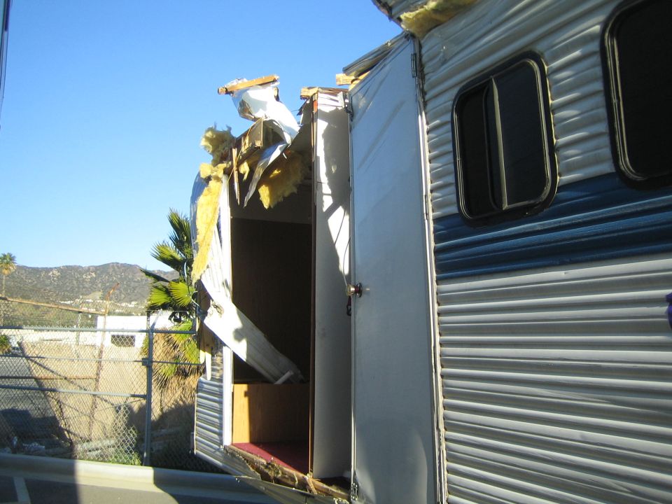 Damaged trailer with roof torn open, exposing insulation and framing