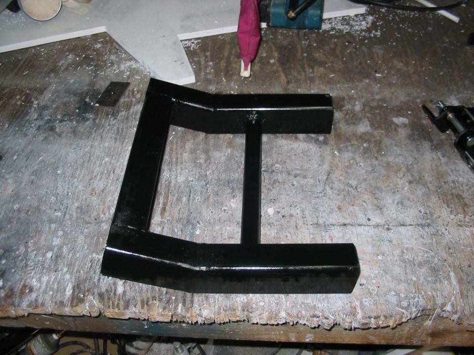 Black metal bracket with a central support bar, resting on a cluttered workbench