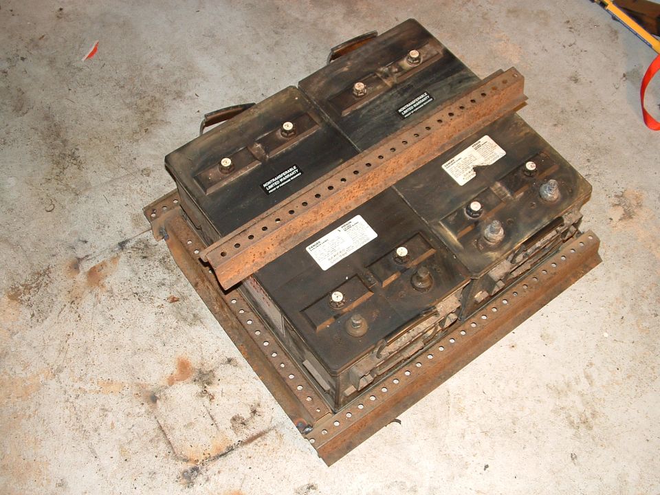 Rusty stacked metal battery boxes or relay assemblies with labels sitting on garage floor