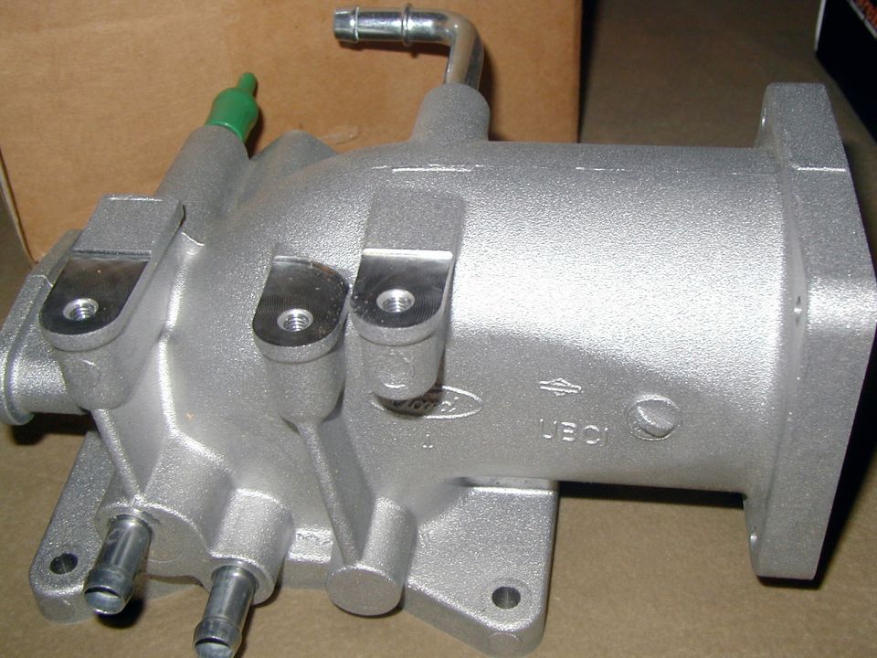 Refinished aluminum Ford intake plenum on cardboard, oval casting mark and vacuum ports visible
