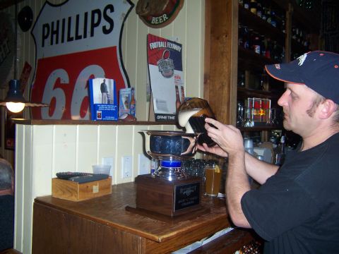 1985 Ford LTD Crown Victoria - A man pours beer into a trophy on a bar counter. A Phillips 66 sign is visible on the wall.