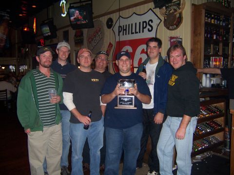 1985 Ford LTD Crown Victoria - A group of men pose for a photo while holding a trophy in what appears to be a bar or restaurant setting.
