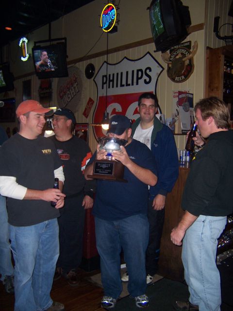 1985 Ford LTD Crown Victoria - A group of men celebrate with a trophy in a bar decorated with various signs and memorabilia.