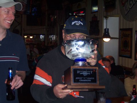 1985 Ford LTD Crown Victoria - A man proudly holds a championship trophy in a dimly lit establishment.