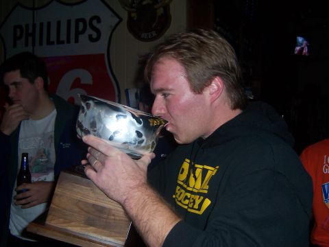 1985 Ford LTD Crown Victoria - A man celebrates by drinking from a trophy, with a friend looking on in the background.