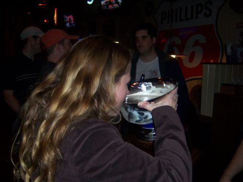 1985 Ford LTD Crown Victoria - People gather in a bar, with one person drinking from a large bowl while a Phillips 66 sign is visible in the background.
