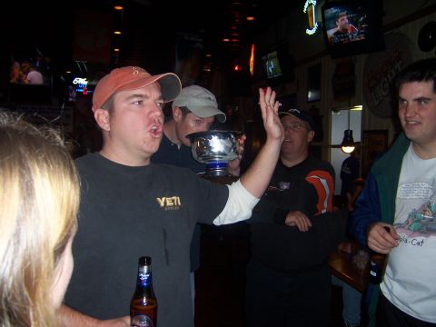 1985 Ford LTD Crown Victoria - People gather in a bar, with one man holding a trophy and others watching.