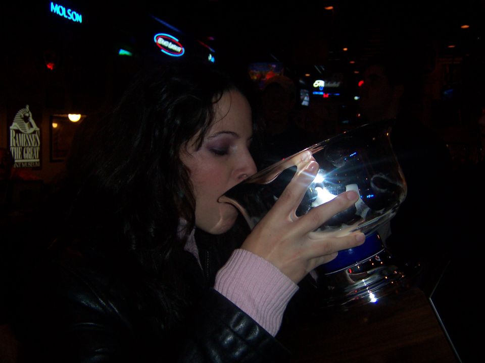 Woman drinking from a large trophy in a dimly lit bar with neon signs