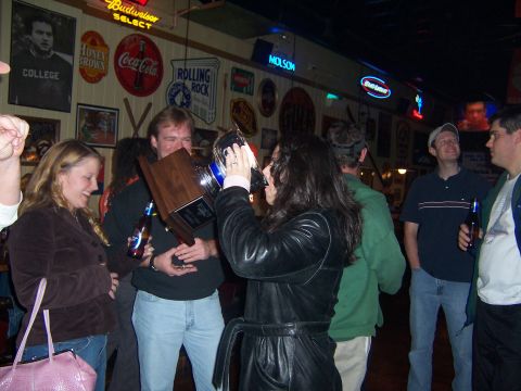 1985 Ford LTD Crown Victoria - A group of people celebrate with a trophy in a bar decorated with neon signs and memorabilia.