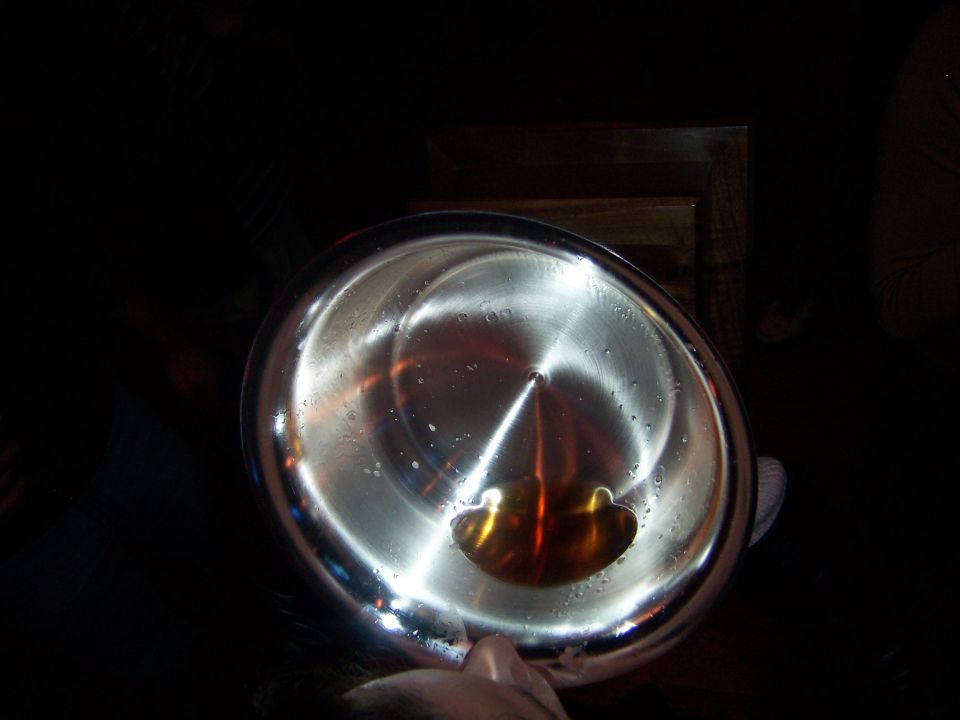 Metal bowl with amber liquid and water droplets, lit from the side