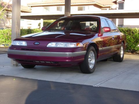 1992 Ford Crown Victoria - A maroon 1992 Ford Crown Victoria is parked outside, showing its front 3/4 view with a police light bar visible through the windshield.