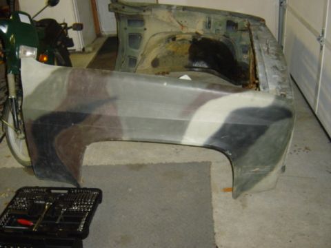 1987 Suzuki Samurai - A camouflage fender is shown next to a motorcycle and a toolbox in a garage.