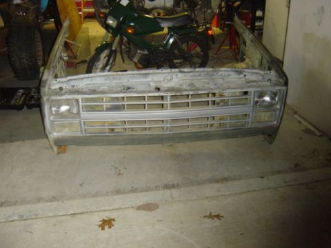 1987 Suzuki Samurai - Front clip of a truck, likely from the 1980s, with a motorcycle in the background.