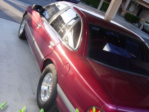 1992 Ford Crown Victoria - A maroon sedan with chrome wheels and drag tires is parked on a concrete surface.