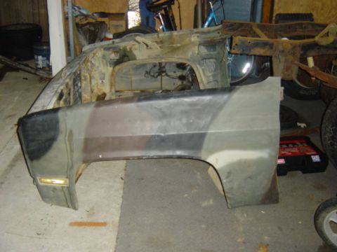 1987 Suzuki Samurai - A disassembled vehicle front fender with camouflage paint and exposed chassis components are visible in a workshop setting.