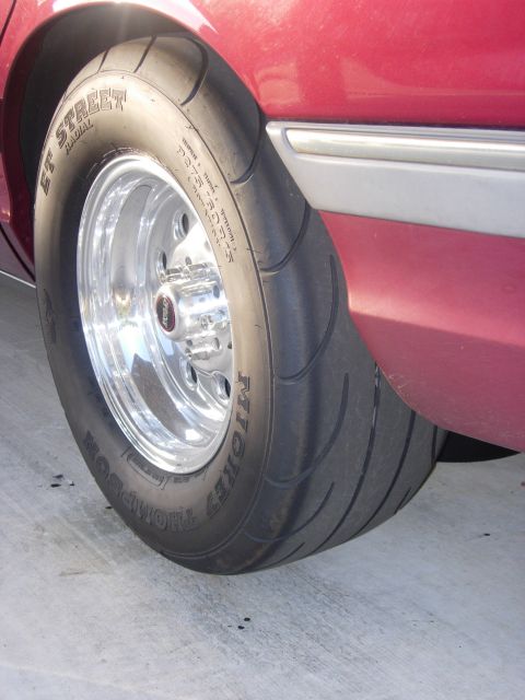 1992 Ford Crown Victoria - Close-up of a red car's rear wheel and tire assembly, showing custom drag racing tires.