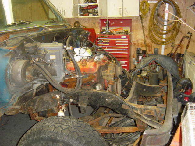 Vehicle engine bay with exposed engine, chassis, and tire. Blue body panel visible