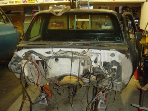 1987 Suzuki Samurai - A disassembled truck cab sits in a garage, revealing its empty engine compartment and wiring.