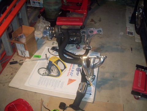 1997 Ford Probe - Aftermarket turbocharger and exhaust manifold components are displayed on a garage floor.