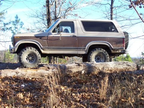 1982 Ford Bronco - This two-tone Ford Bronco is positioned on a fallen tree in a wooded area.