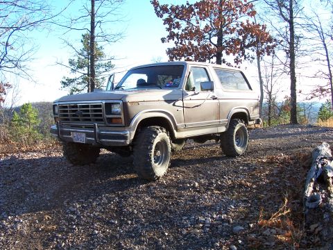 1982 Ford Bronco - This lifted Ford Bronco is parked on a gravel road with trees in the background.