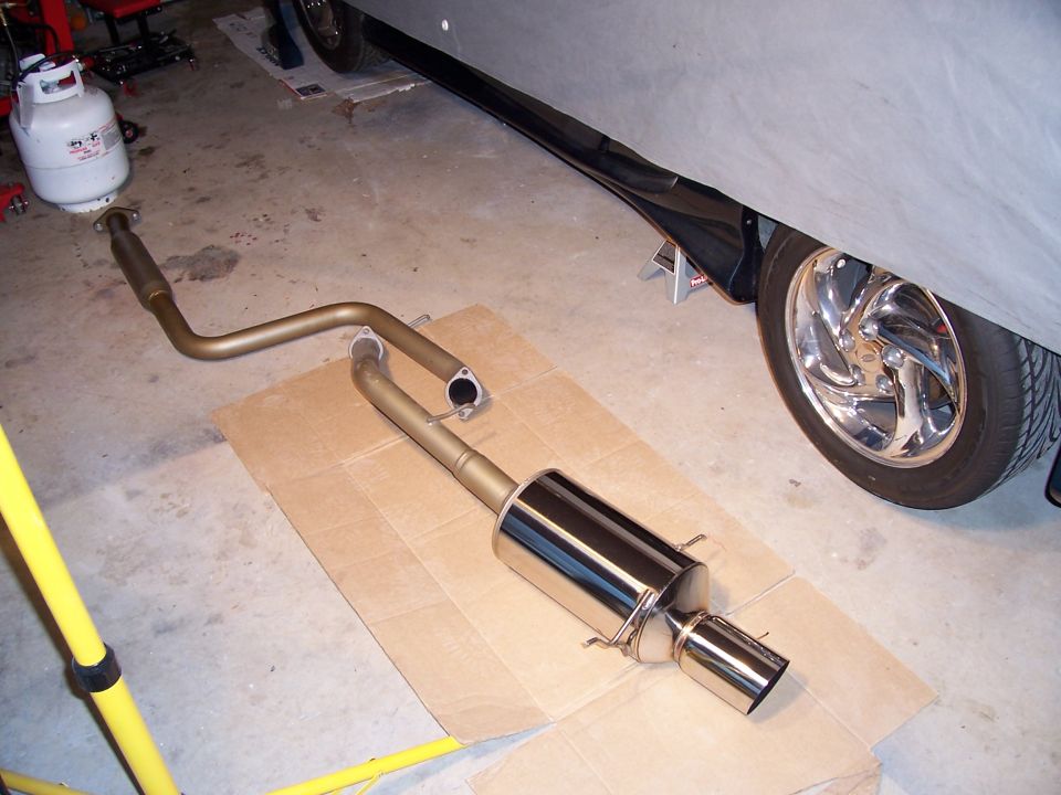 car covered with a tarp, with a new exhaust system laid out on cardboard next to it