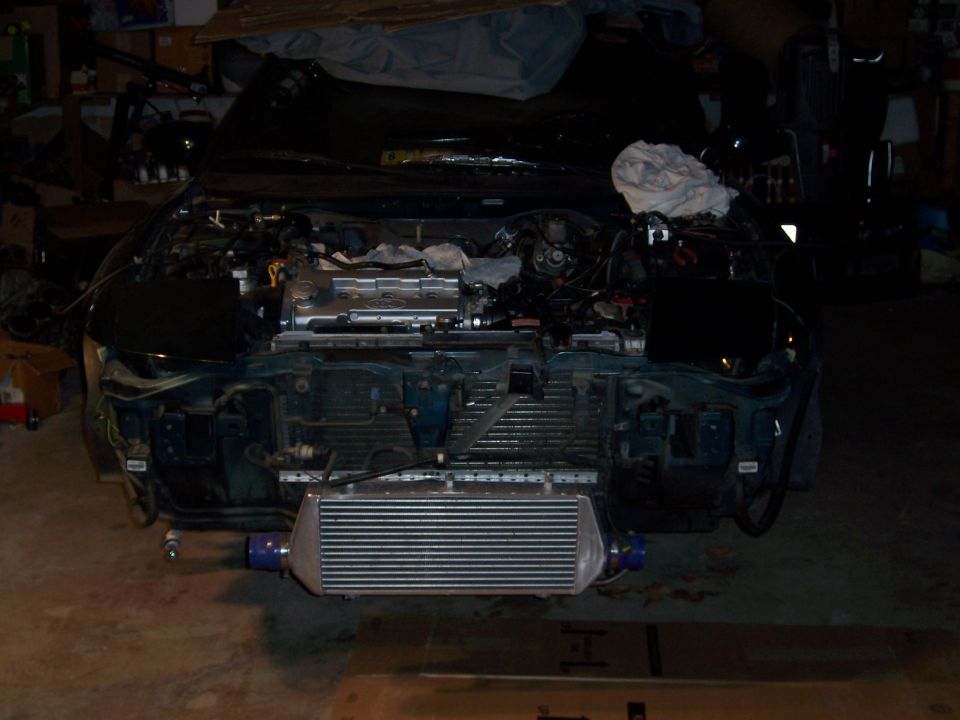 Car engine bay with front bumper removed, showing an intercooler and exposed engine components