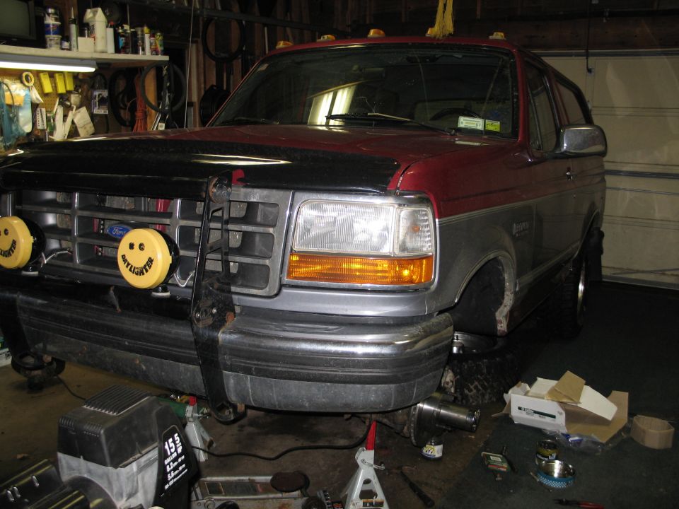 1995 Ford Bronco front end with custom bumper and yellow smiley face lights, jacked up for service