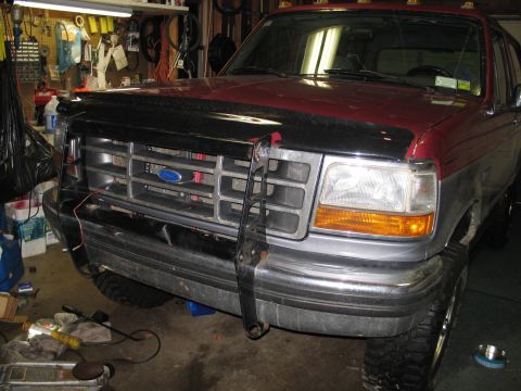 1995 Ford Bronco - A two-tone Ford F-Series truck is parked in a garage, showing its front grille and bumper.
