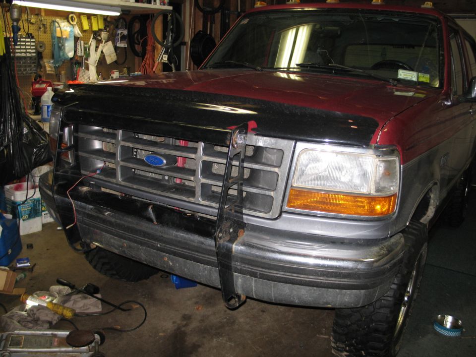 Front view of a red and gray Ford F-Series truck in a garage. It has a black bug deflector and a chrome grille guard