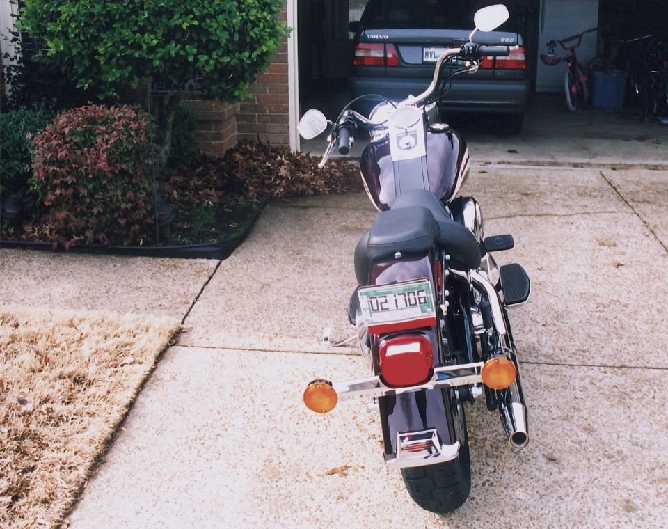 Rear view of dark Harley-Davidson Softail motorcycle in driveway with Volvo wagon in garage behind