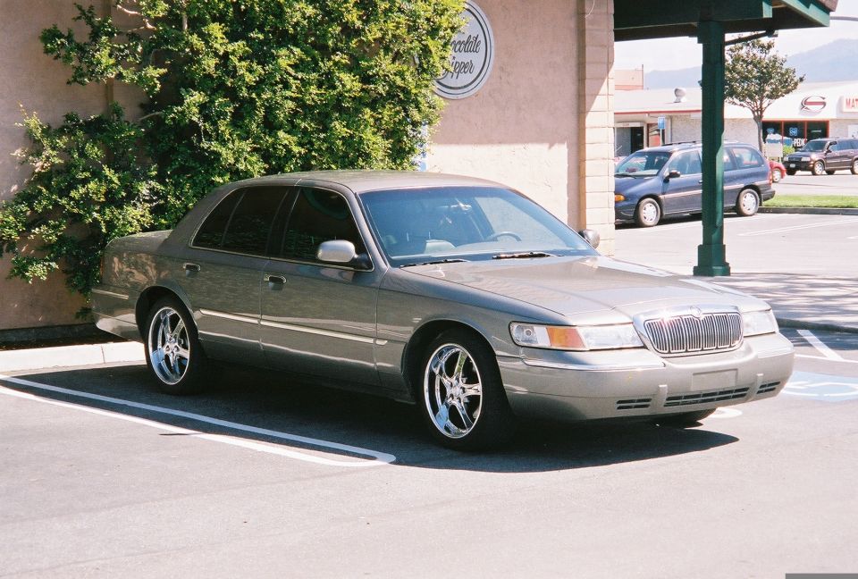 Gray 2000 Mercury Grand Marquis parked in a lot, chrome wheels, slight damage on front bumper