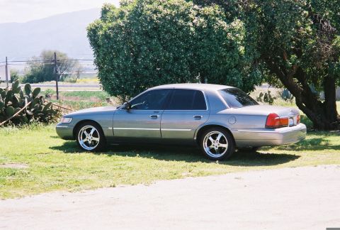 2000 Mercury Grand Marquis - A silver 2000 Mercury Grand Marquis sedan is parked on a grassy area next to a large tree.